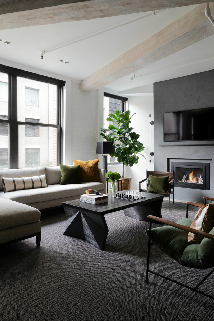 A modern living room with large windows, a sectional sofa, armchairs, a black coffee table, a fireplace, a wall-mounted TV, green accents and a large potted plant.